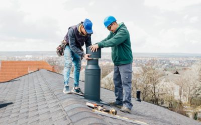 two professional masters Roofer construction workers repairing chimney on grey slate shingles roof of domestic house, sky background with copy space.